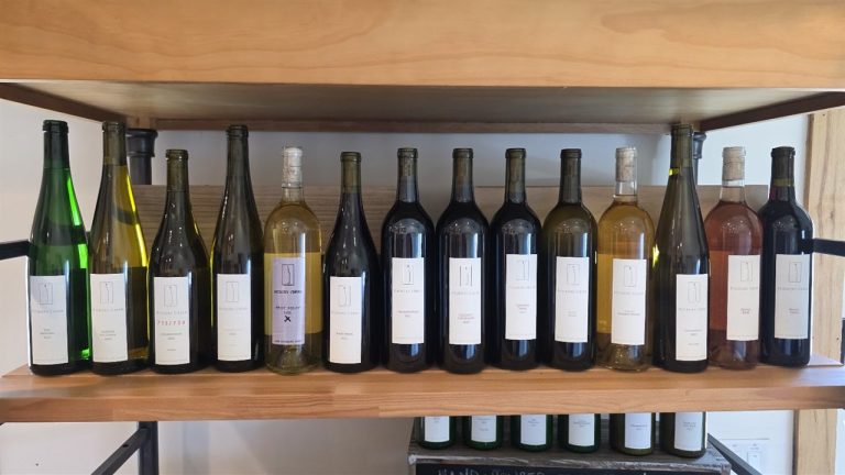 A row of Hickory Creek Winery bottles on a wood shelf in their Buchanan, Michigan tasting room, including the winery's Riesling, Chardonnay, Traminette, Chambourcin, Pinot Noir, and rose